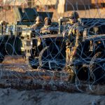 National Guard soldiers with military vehicles behind barbed wire.